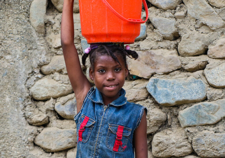 A young girl, carrying a bucket of water on her head in Haut Limbe, Haiti. 